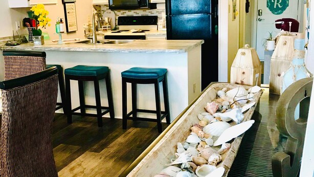 Een keuken met witte kasten, een zwarte koelkast en een centraal kookeiland met krukken.