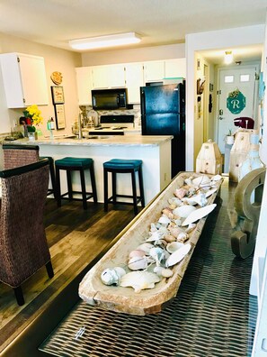 Cocina con armarios blancos, refrigerador negro y una isla central con taburetes.