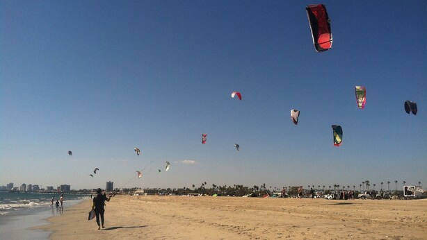 A beach with people walking and kites flying in the sky.