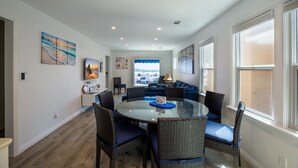 A dining area with a glass table surrounded by wicker chairs, a blue sofa, and a view of a parking lot through a window.