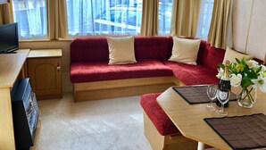 Interior acogedor de una autocaravana con un sofá rojo, una mesa de madera con dos copas de vino y un televisor sobre un mueble de madera.