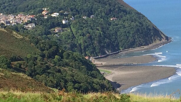 Un paisaje costero con una colina cubierta de vegetación y una playa con olas.