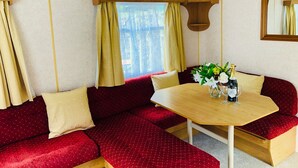 Una habitación acogedora con una mesa de madera, asientos tapizados en rojo y una ventana con cortinas.