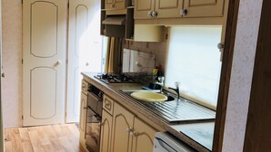 Una cocina compacta con suelo de madera, armarios blancos, una estufa a gas y un refrigerador.