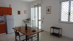 A kitchen with a wooden table, chairs, a refrigerator, and a vase with flowers. - VersoSud - Apartment Vicino Spiaggia 04 (Ugento)