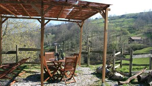 An outdoor seating area with a wooden pergola, a table, and chairs. - Charming cottage in the valleys pasiegos. Stunning views of the mountains. (San Roque de Riomiera)
