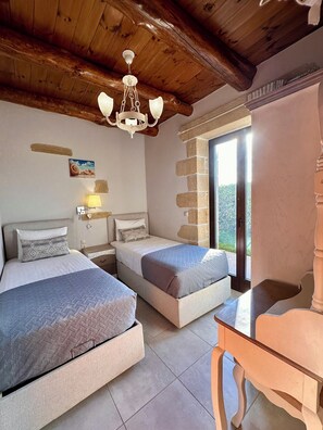 A bedroom with two beds, a wooden ceiling, a chandelier, a window with a view, and a small table.