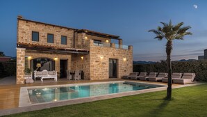A two-story stone house with a swimming pool, outdoor seating, and a palm tree.