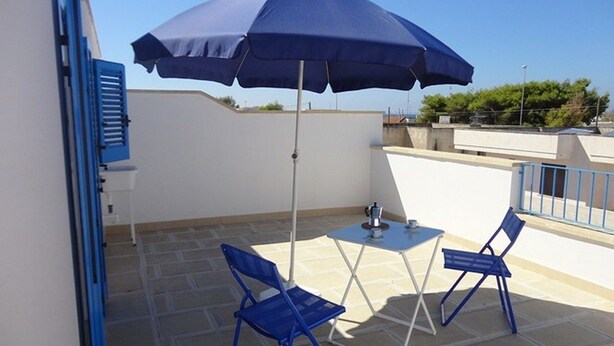 Un petit espace extérieur aménagé avec une table et deux chaises bleues, un parasol bleu et un mur blanc.