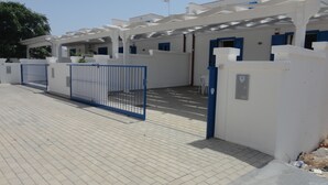 Un parking clos, avec un bâtiment blanc et des volets bleus.