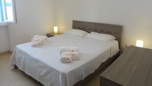 Un lit bien fait, avec du linge de lit blanc et deux oreillers, une table de chevet avec une lampe et une petite table en bois.