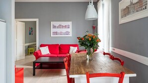 Ett modernt vardagsrum med en röd soffa, ett matbord i trä och en vas med blommor.