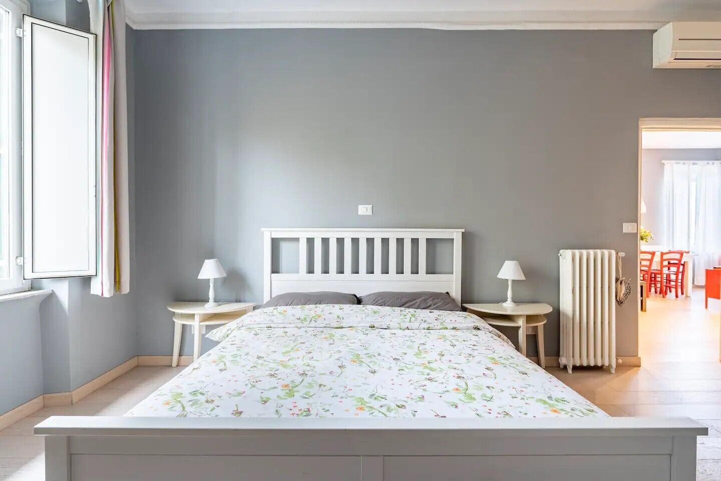 A bedroom with a bed, two bedside tables, a radiator, and a window with curtains.