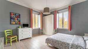 Ett sovrum med en säng, en byrå, en stol, en tv och ett fönster med gardiner.