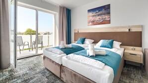 Habitación de hotel con dos camas, un ventanal con vistas, un cuadro en la pared y una mesita de noche con lámpara.