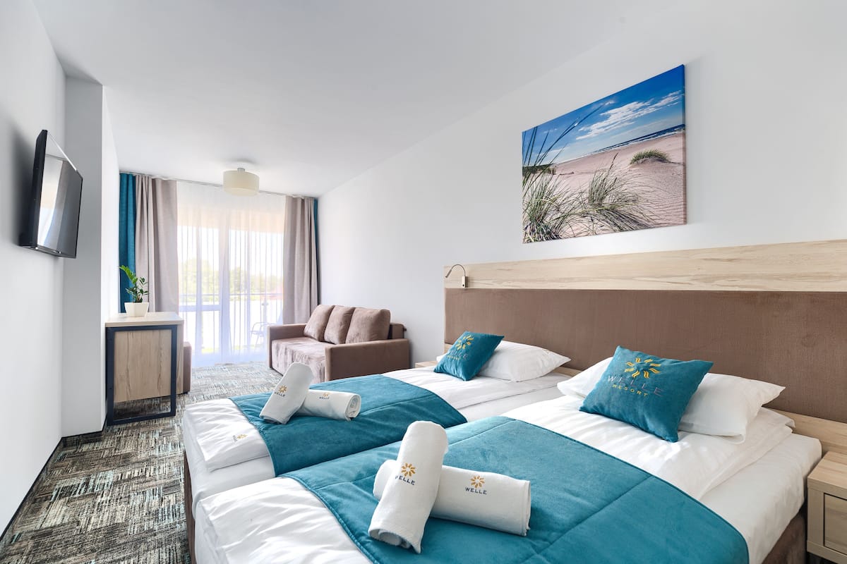 A hotel room with two beds, a TV, a desk, and a window with curtains.