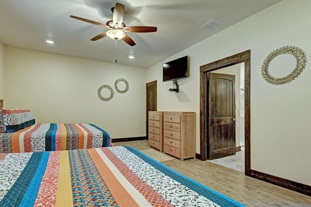 A bedroom with two beds, a ceiling fan, a TV, wooden cabinets, and a door leading to another room.