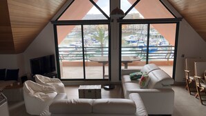 A spacious living room with a large window overlooking a marina, a white sofa, a coffee table, and a TV. - HEC Beach Apartment Marina Vilamoura, sea side, pool, golf, beach, boat trips,  (Quarteira)