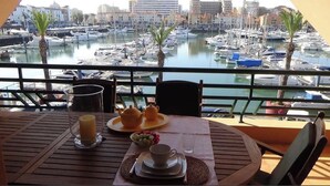 A balcony with a table set for breakfast, overlooking a marina with boats and buildings. - HEC Beach Apartment Marina Vilamoura, sea side, pool, golf, beach, boat trips,  (Quarteira)