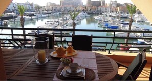 Un balcón con una mesa dispuesta para el desayuno, con vistas a una marina con barcos y edificios.