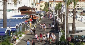 Eine belebte Straße mit Fußgängern, Palmen und Häusern mit Geschäften.