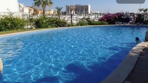 A swimming pool with clear blue water, surrounded by greenery and buildings in the background. - HEC Beach Apartment Marina Vilamoura, sea side, pool, golf, beach, boat trips,  (Quarteira)