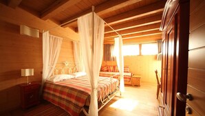 A wooden cabin bedroom with a four-poster bed, a nightstand, a wardrobe, and a window with curtains. - Le Case dei Baff (Ardenno)