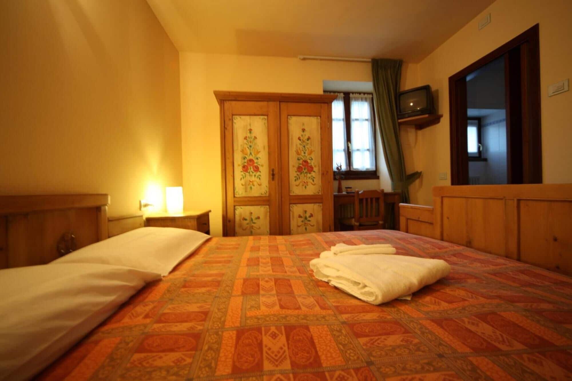 A hotel room with a large bed, a wooden wardrobe, a desk, and a television on the wall.