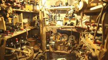 Une cave encombrée, remplie de barils en bois, de bouteilles et de divers outils.