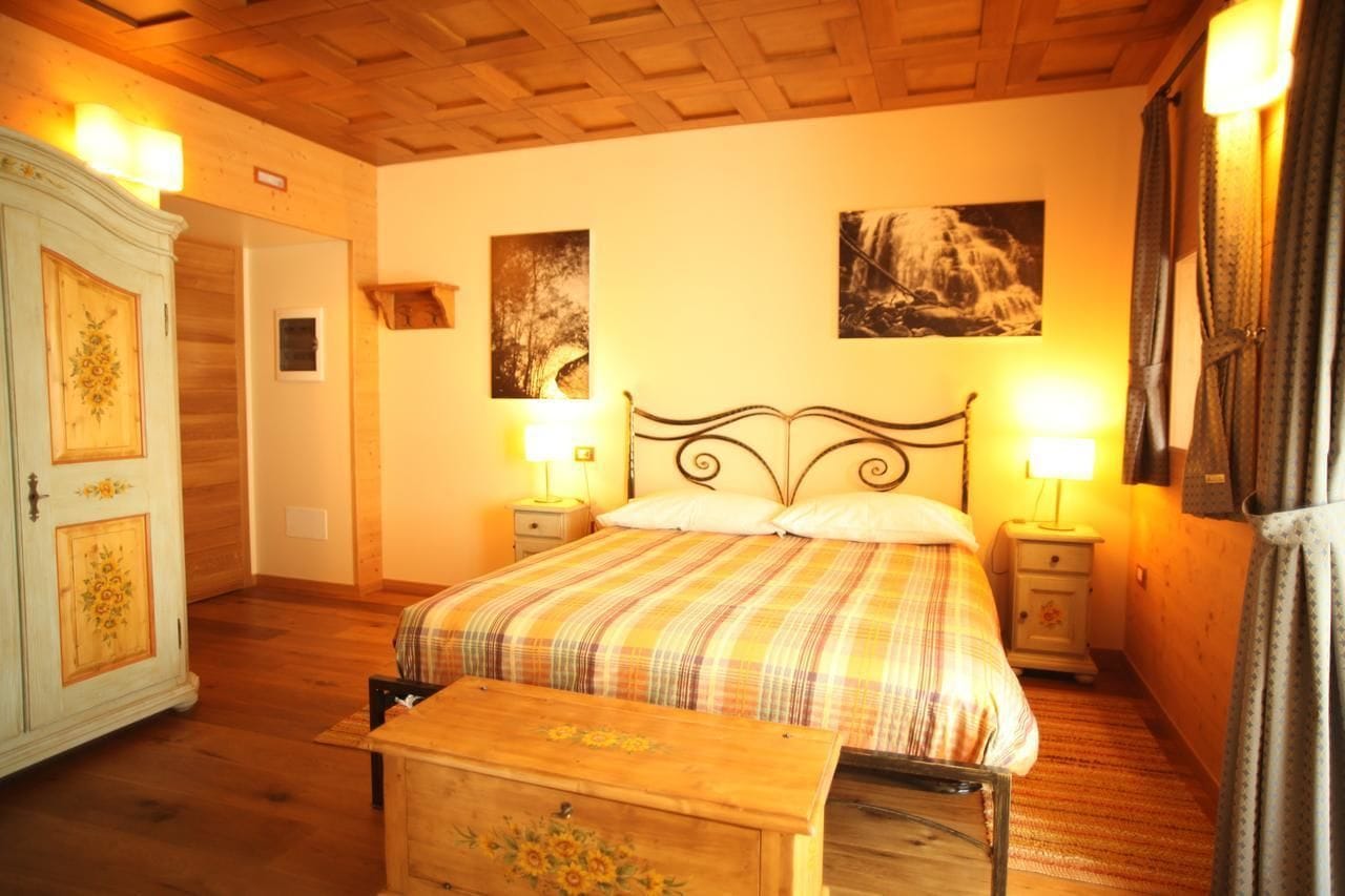 Un dormitorio con cama, mesitas de noche, armario y dos lámparas de pared.