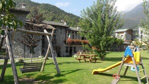 A playground with swings and a slide, a picnic table, and stone buildings with balconies. - Le Case dei Baff (Ardenno)