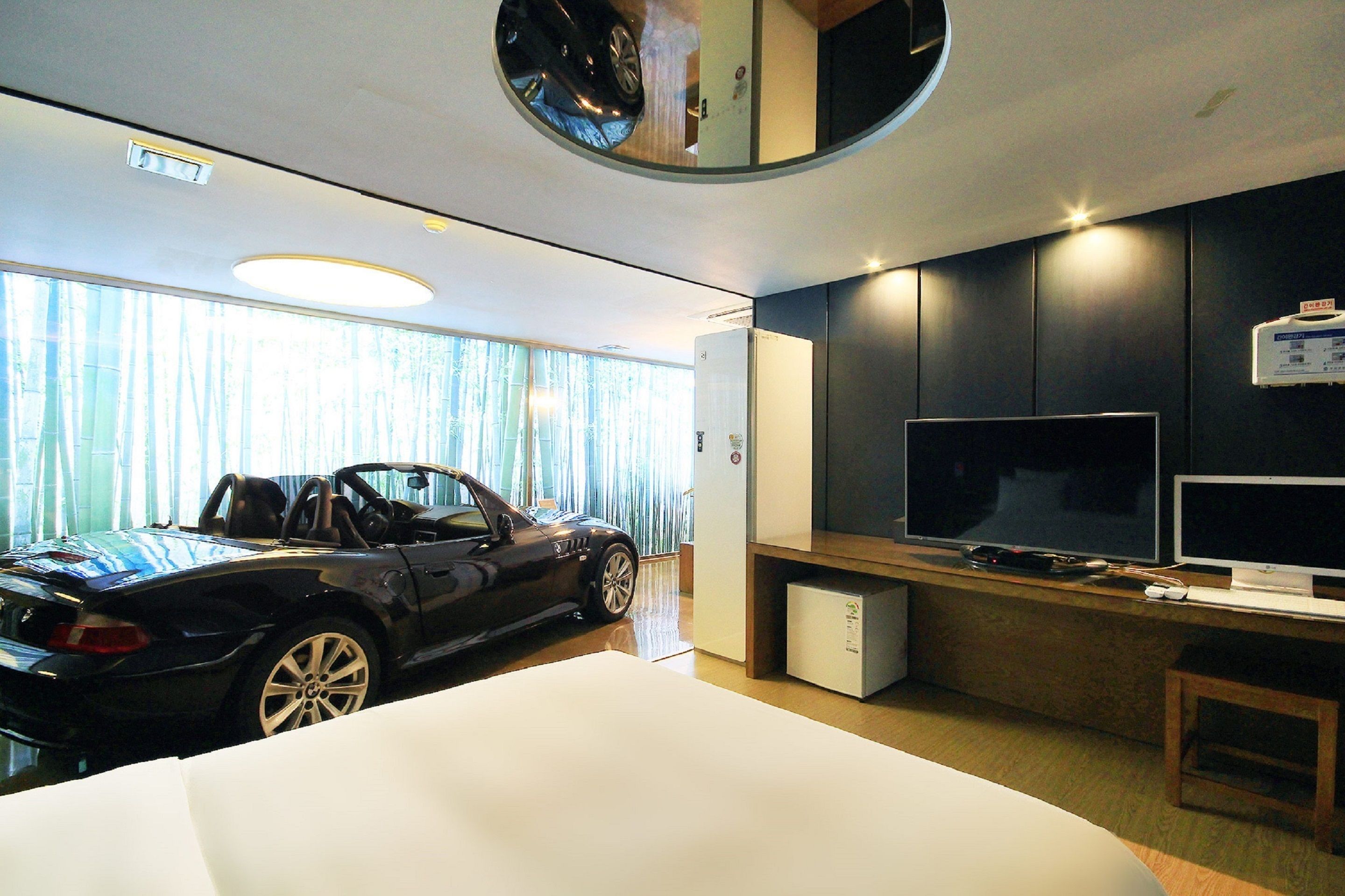 A modern hotel room with a convertible sports car, a flat-screen TV, and a compact refrigerator.