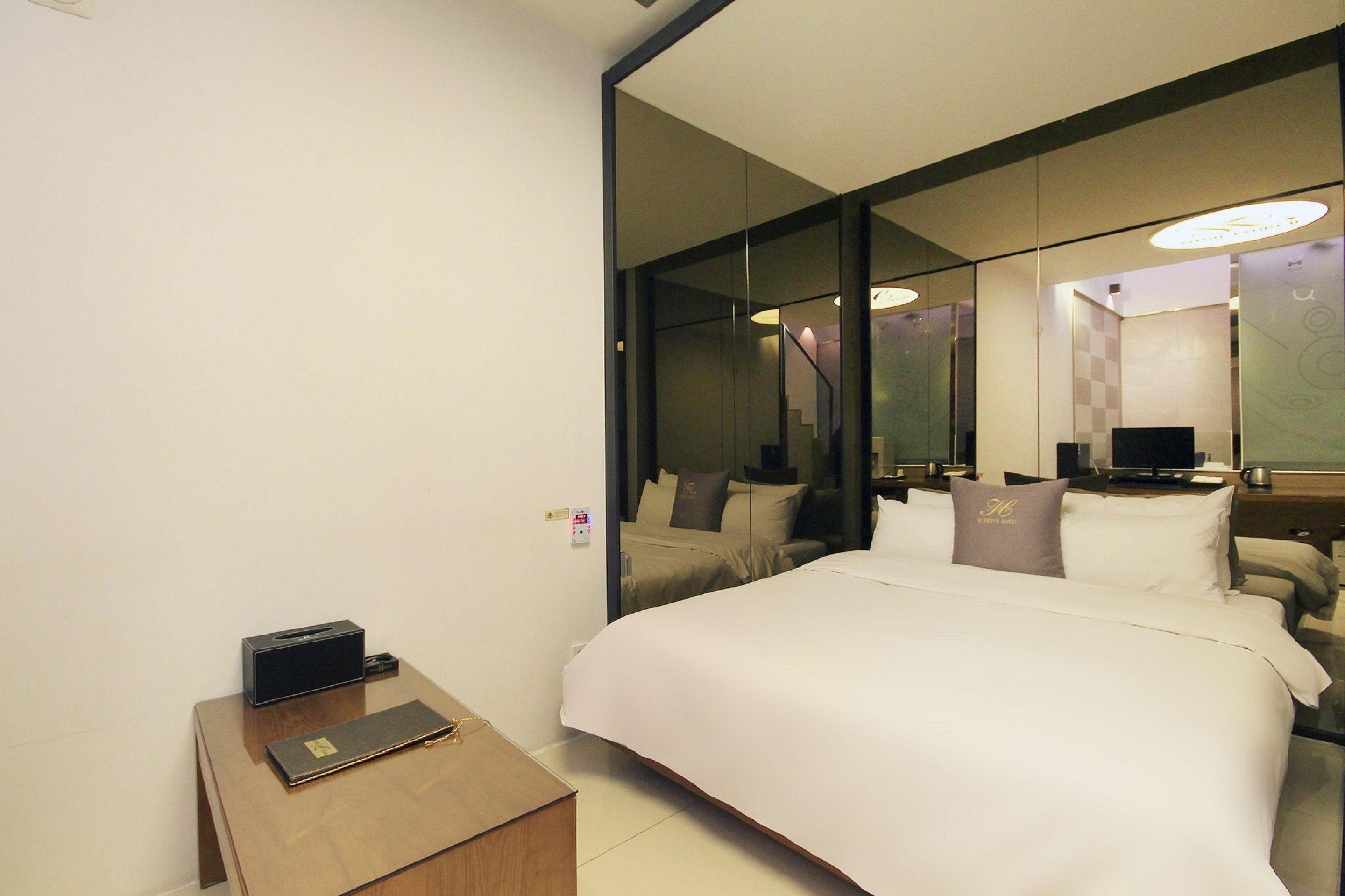A hotel room with a large bed, a bedside table with a lamp, a mirror, and a television.