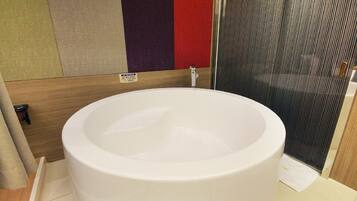 Una bañera blanca grande en un baño con piso de madera y un panel de pared rojo y morado.