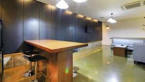 Zona de bar moderna con mostrador de madera, taburetes negros y lámparas colgantes.
