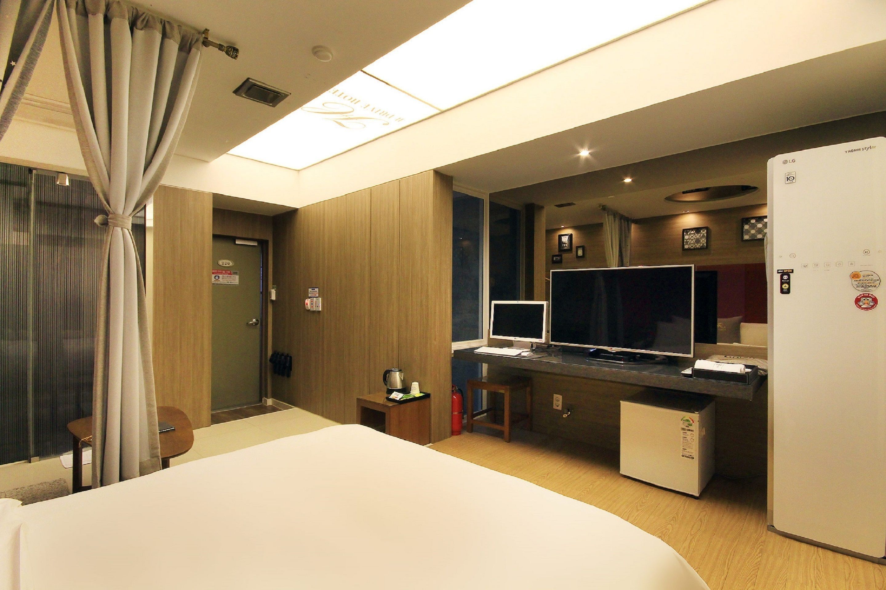 Ein Hotelzimmer mit einem Bett, einem Schreibtisch mit Computer, einem Kühlschrank und einem Fenster mit Vorhängen.