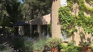 A building with a stone facade partially covered in ivy, surrounded by gravel and potted plants. - Lou Ventoulet (Mouries)