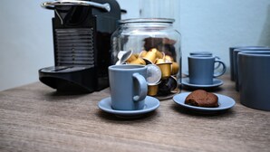 A coffee setup with a coffee maker, a glass jar with coffee beans, and several blue cups and saucers on a wooden table.