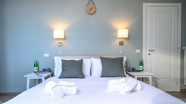 A neatly made bed with pillows, a clock on the wall, and two bedside tables with bottles and cups.