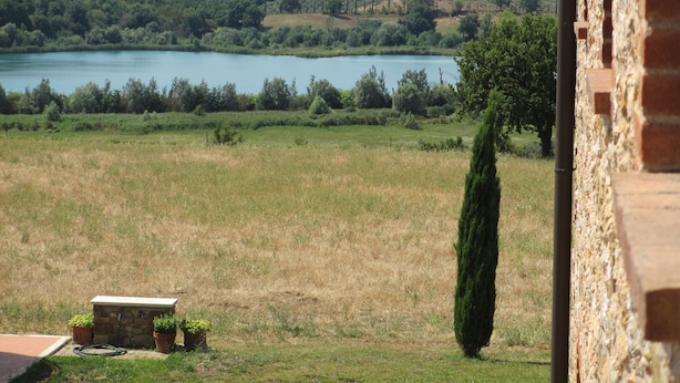Une vue sur un lac entouré de collines, un mur de briques et une pelouse bien entretenue avec un banc et des plantes en pot.