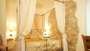 Une chambre avec un mur en pierre, un cadre de lit en métal et un lit à baldaquin agrémenté de rideaux.
