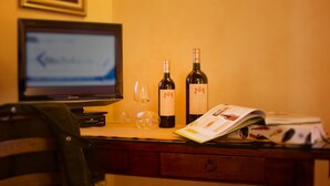Un bureau avec un écran d’ordinateur, deux bouteilles de vin, un verre à vin et un magazine.