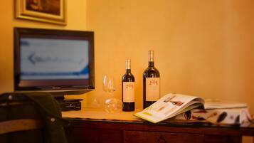 Una scrivania con un monitor del computer, due bottiglie di vino, un bicchiere da vino e una rivista.