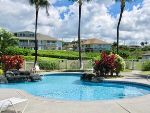 A swimming pool with lounge chairs, palm trees, and a building in the background. - Oceanview Townhome w/ Pool Near Beaches & Shops (Kailua-Kona)