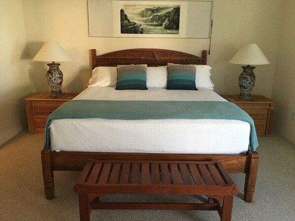 A neatly made bed with a wooden headboard, two bedside tables with lamps, and a framed picture on the wall.