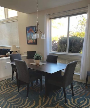 A dining area with a dark wooden table, four chairs, a hanging light fixture, and a window with curtains. - Oceanview Townhome w/ Pool Near Beaches & Shops (Kailua-Kona)