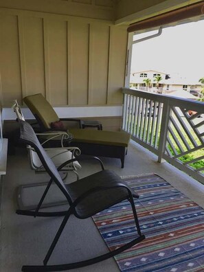 A balcony with two lounge chairs and a patterned rug.