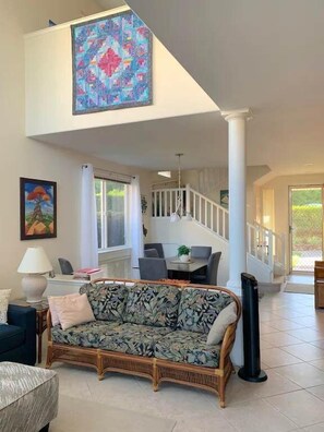 A spacious living room with a high ceiling, a large painting, a dining area, and a staircase leading to another level. - Oceanview Townhome w/ Pool Near Beaches & Shops (Kailua-Kona)