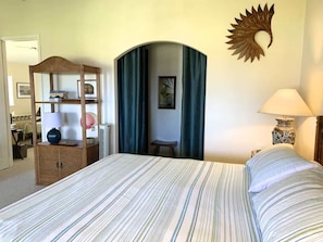 A bedroom with a bed, a wooden cabinet, a desk, a chair, a lamp, and a decorative wall piece.
