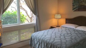 A hotel room with a bed, a nightstand, a lamp, a window with curtains, and a painting on the wall.